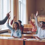Multiethnic group of young people is listening to teacher and smiling then raising hands. Pupils and tutors concept.
